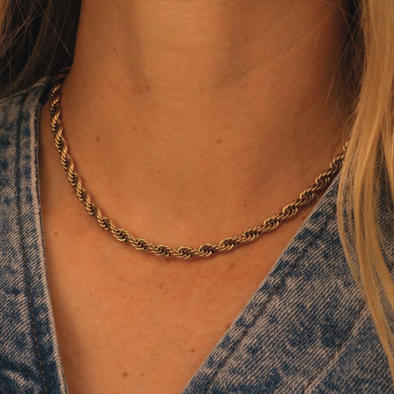 Gold chain necklace worn by a person with a denim jacket